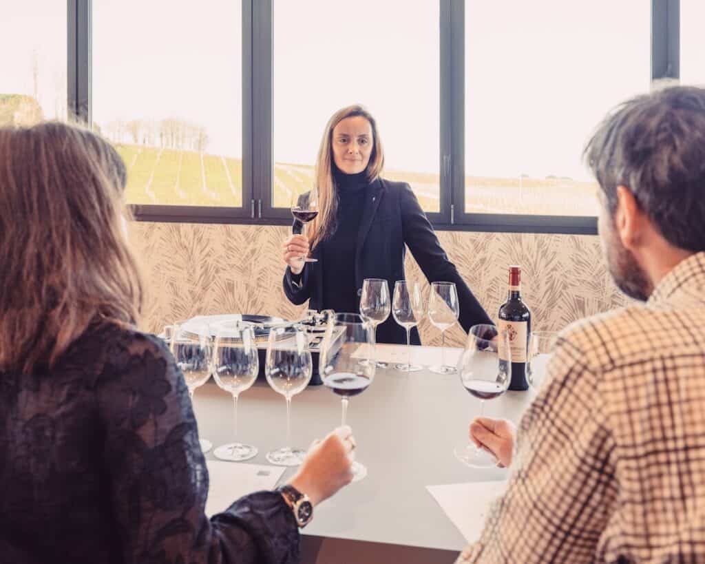 Dégustation guidée dans un domaine viticole de Bordeaux, où un couple découvre un vin rouge lors d’une excursion œnologique face aux vignobles.