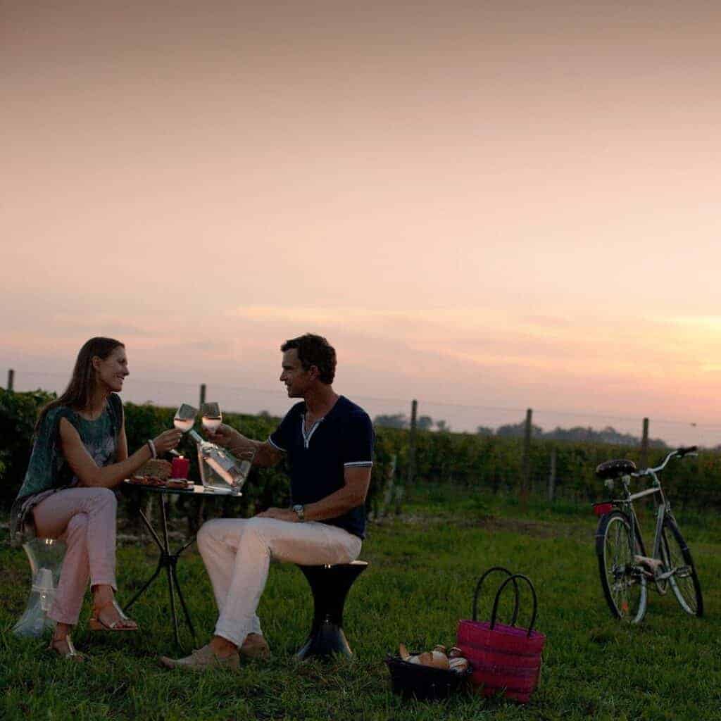 Couple en pique-nique romantique dans les vignes de Bordeaux au coucher du soleil, lors d’un weekend œnologique