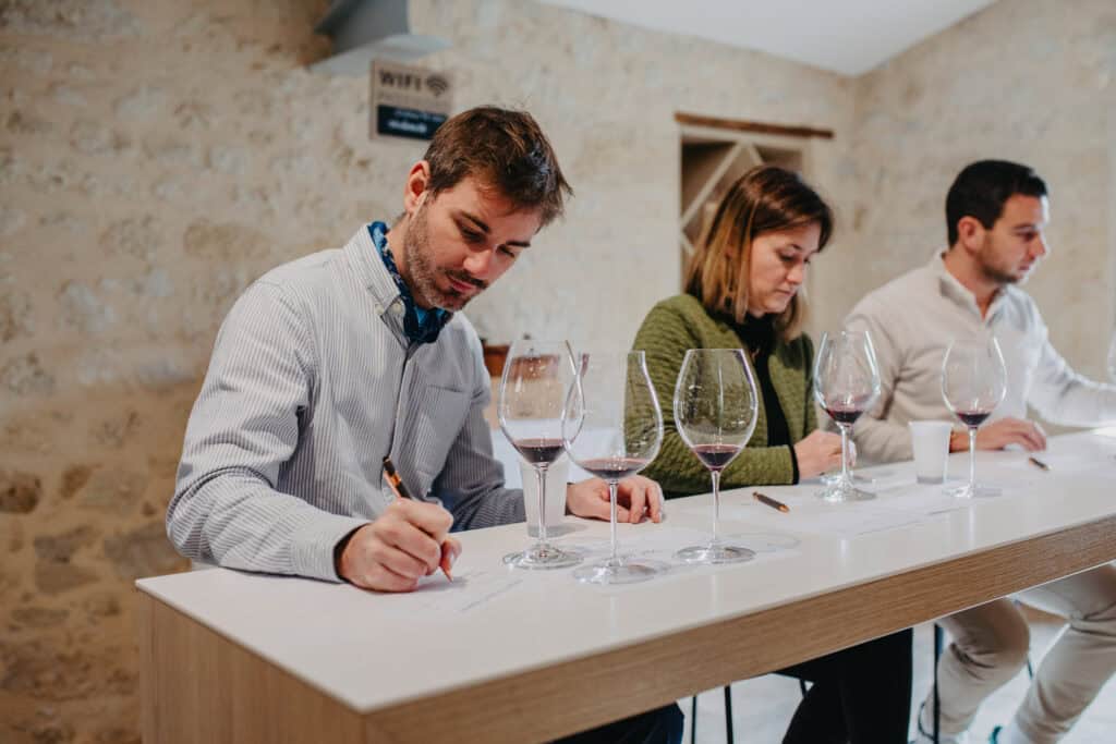 Deux participants assis notant leurs impressions devant des verres de vin lors d’une dégustation.